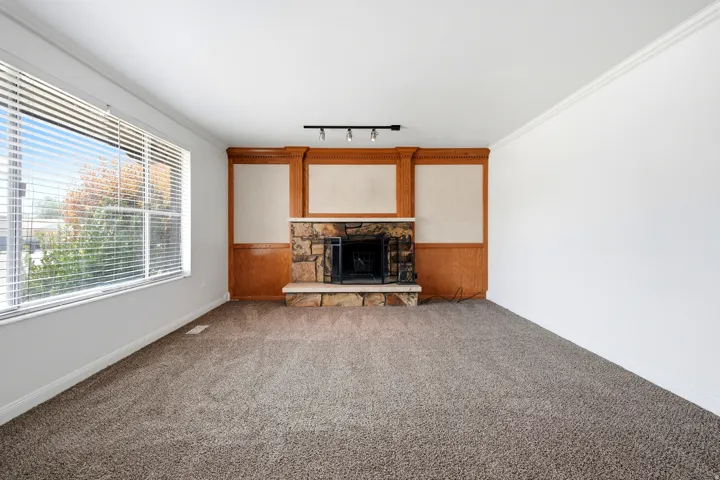 Stone fireplace with wood paneling, large windows, crown molding, and neutral-toned carpeting
