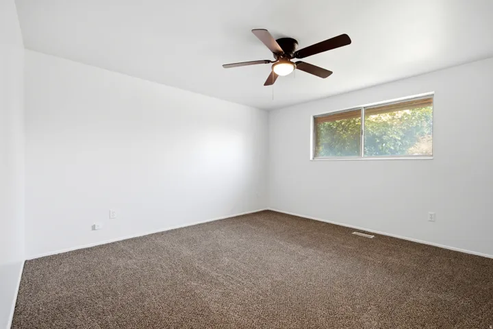 Neutral paint palette and brown carpeting with a ceiling fan and a rectangular window
