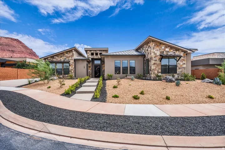 Modern desert landscaping with stone accents and a curved concrete walkway leads to the entry