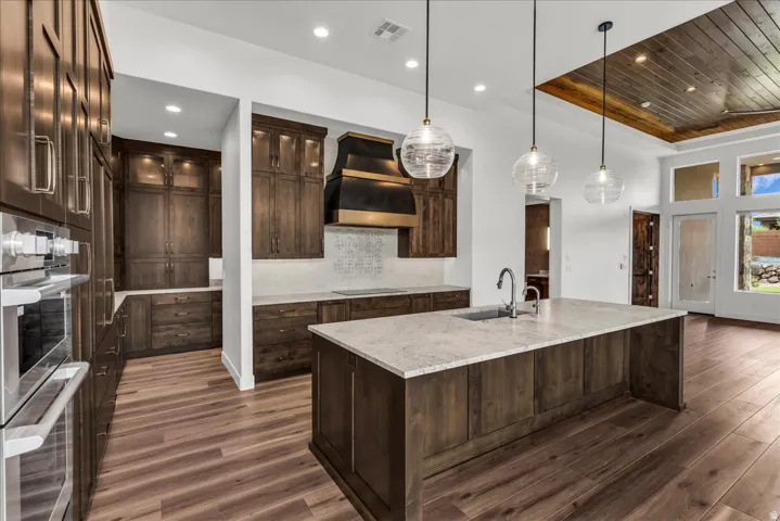 Spacious kitchen featuring an expansive center island with an undermount sink, built-in stainless steel appliances, and wood-finish flooring