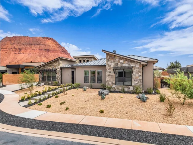 Contemporary architecture featuring stone and stucco exterior finishes, a low-slope roofline, a xeriscaped front yard with decorative rock and plantings, and a paved walkway