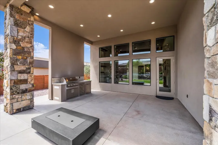 Covered outdoor living area with a built-in barbecue, stone veneer columns, and extensive window-paned doors