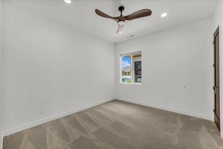 Recessed lighting, ceiling fan with wood-finish blades, and neutral carpet