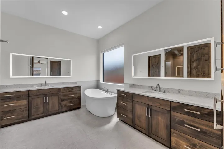 Freestanding soaking tub, dual wood-finish vanities with undermount sinks, and illuminated mirrors