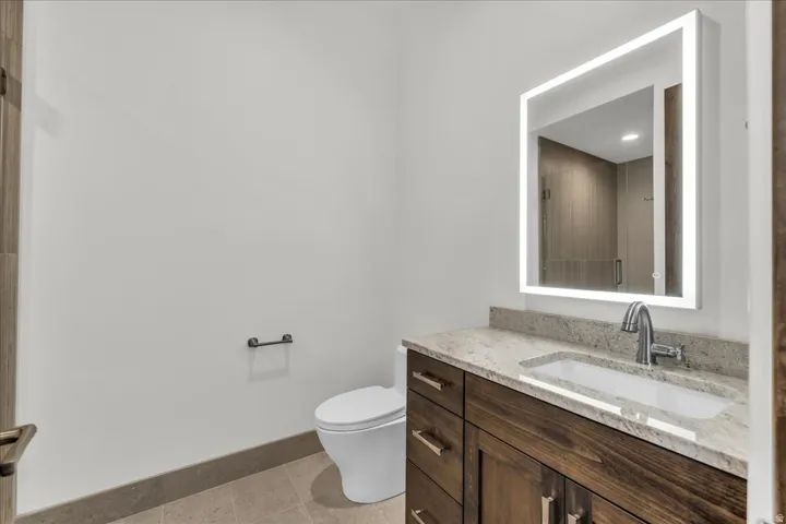 Modern powder room featuring a wood-finish vanity with ample storage, a white ceramic vessel sink, and a polished stone countertop