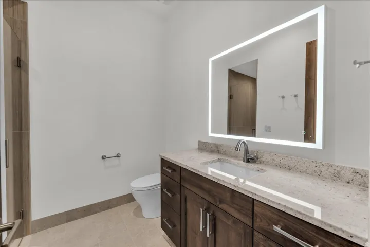 Dark wood-finish vanity with ample storage, light-toned countertop, rectangular undermount sink, and illuminated mirror