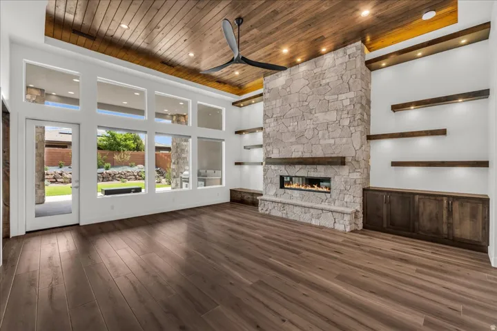 Wood-finish flooring, wood-paneled ceiling, stone-clad fireplace with hearth, built-in shelving with accent lighting, and integrated cabinetry