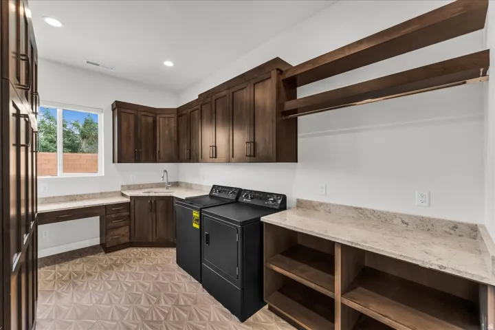 Extensive built-in cabinetry, corner sink with stainless steel faucet, ample counter space, integrated desk area, and patterned tile flooring
