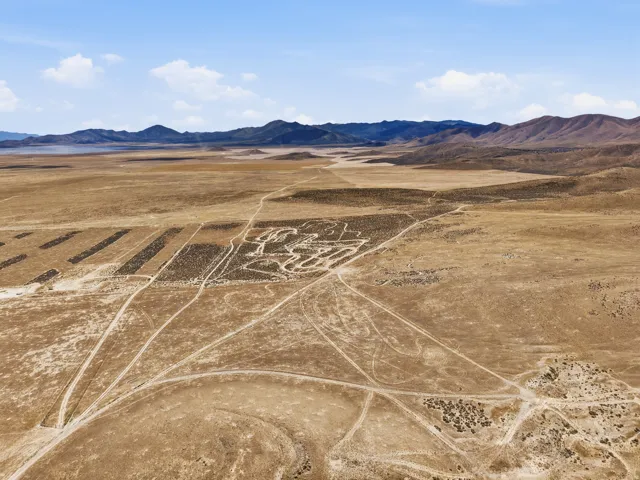 Expansive desert landscape with distant mountains, featuring a network of unpaved tracks and sparse vegetation