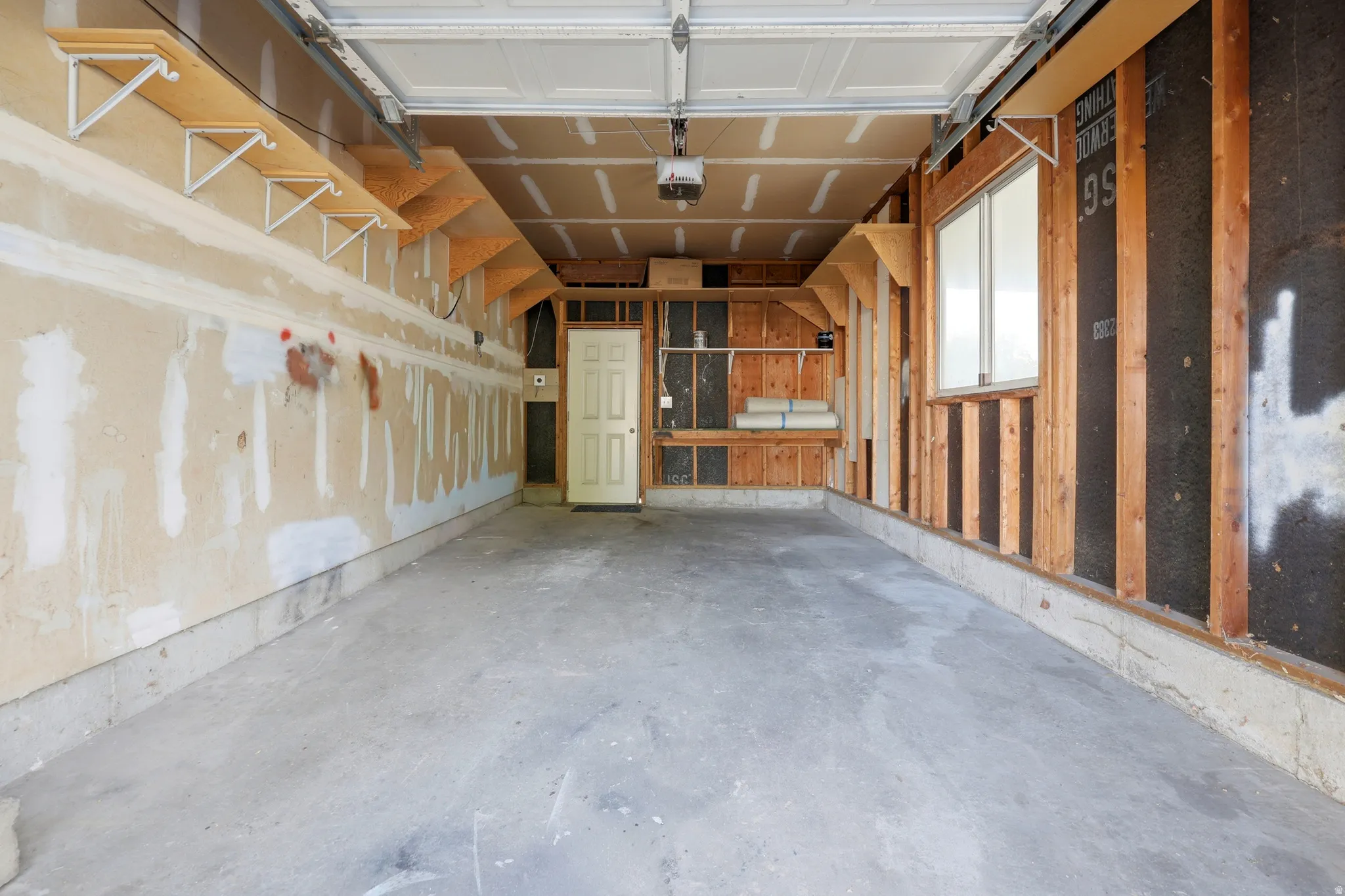 Concrete flooring, built-in shelving, paneled door, single window, exposed wall studs
