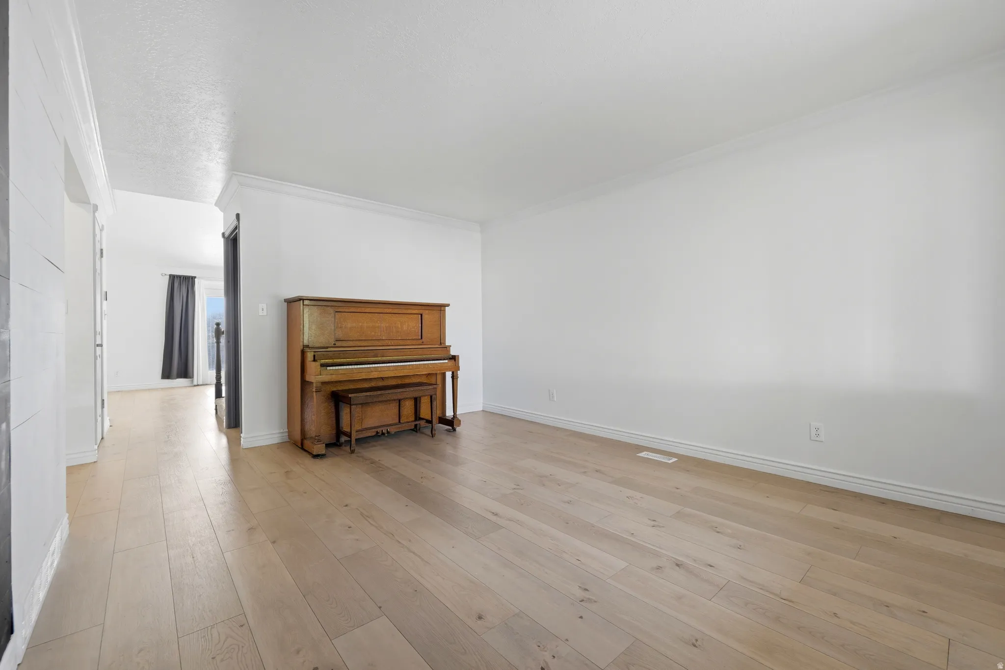 Spacious room featuring light wood-finish flooring, white walls, and abundant natural light