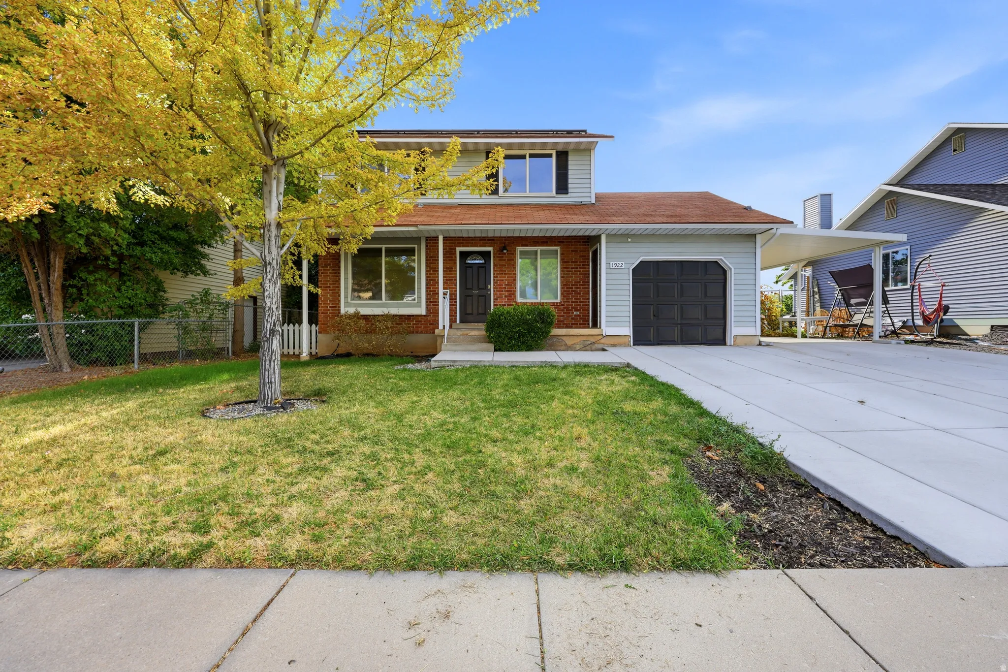 Brick Colonial two-story home featuring a manicured front lawn with mature shade trees, concrete driveway, attached two-car garage, and covered front entry with white trim detailing