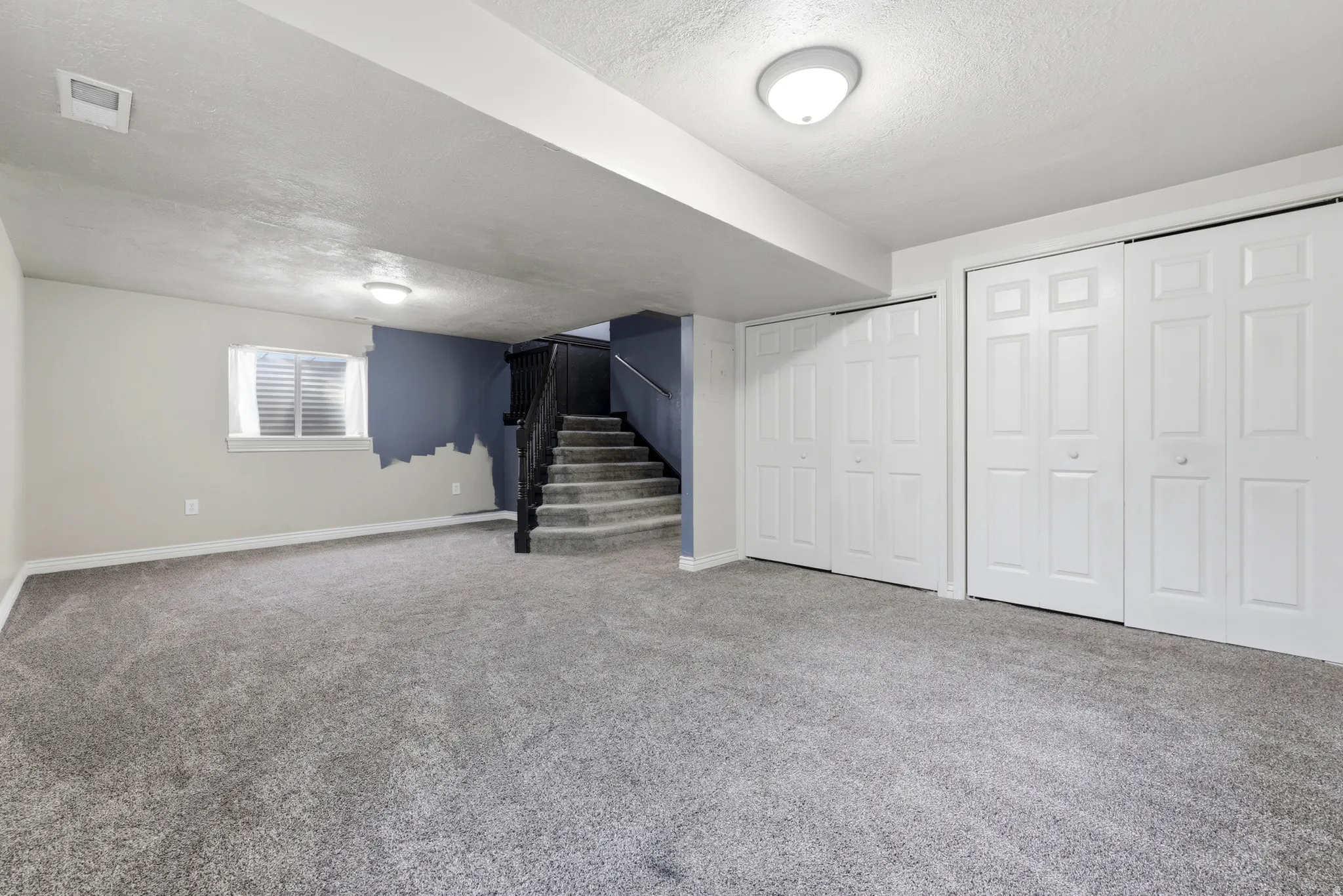 Spacious basement recreation area featuring plush carpeting throughout, white six-panel closet doors, recessed ceiling lighting, and a small window providing natural light