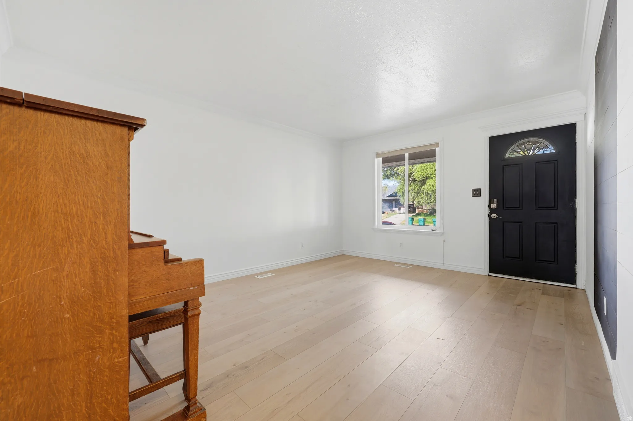 Bright and spacious living area showcasing light wood-finish flooring, white walls, and abundant natural light from a front-facing window