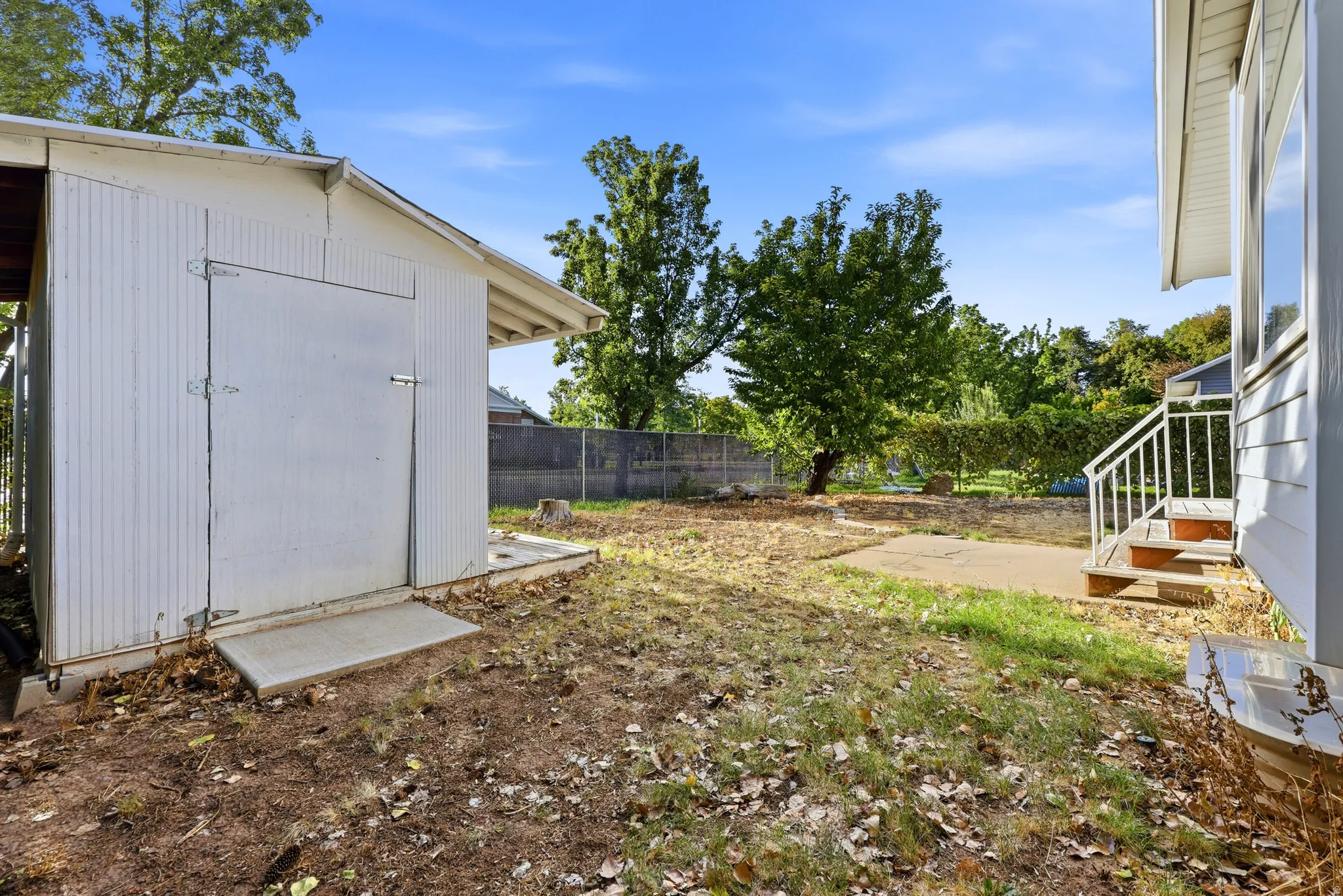 Spacious backyard with mature trees and established landscaping, featuring a utility shed and fenced perimeter