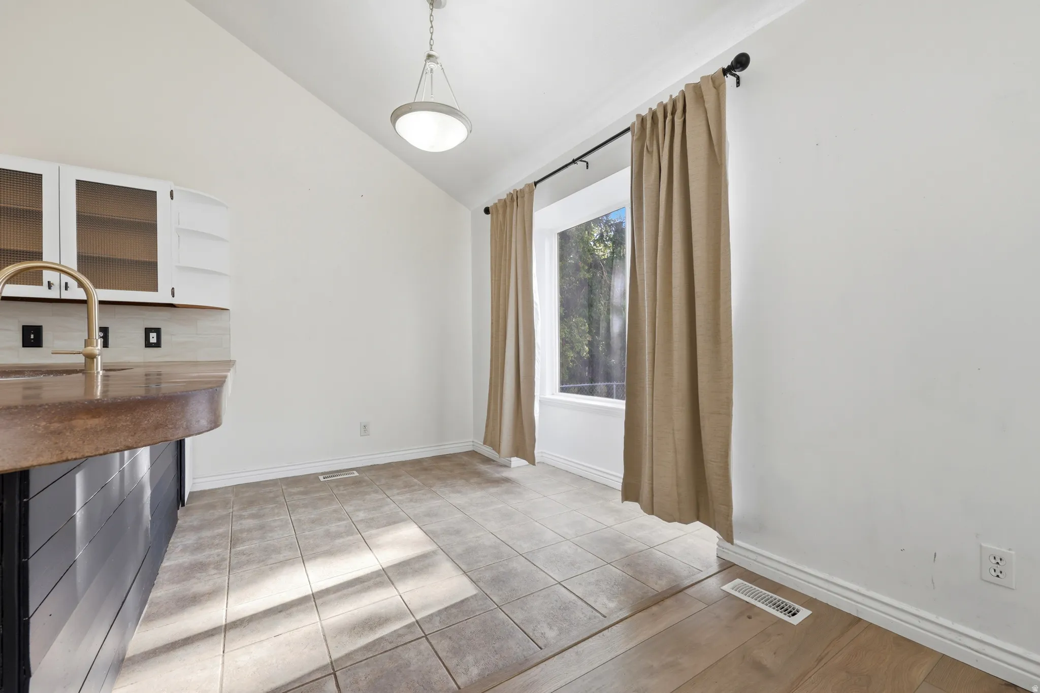 Bright, open kitchen and dining area with tile flooring, stainless steel appliances, wood cabinetry, and abundant natural light from glass sliding doors framed by neutral curtains