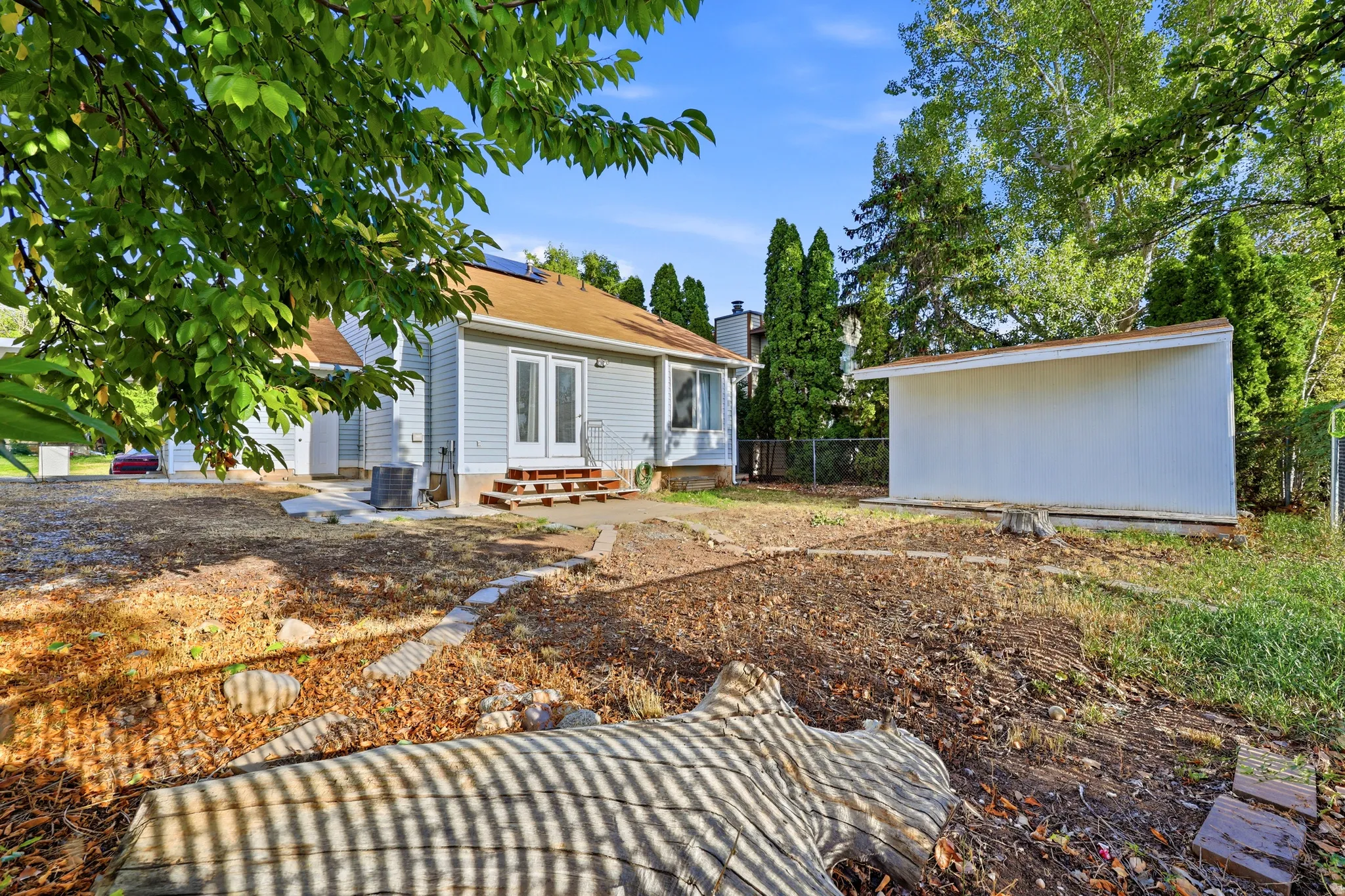 Spacious backyard with mature tree coverage and established landscaping, featuring a detached garage structure and newly prepared grounds