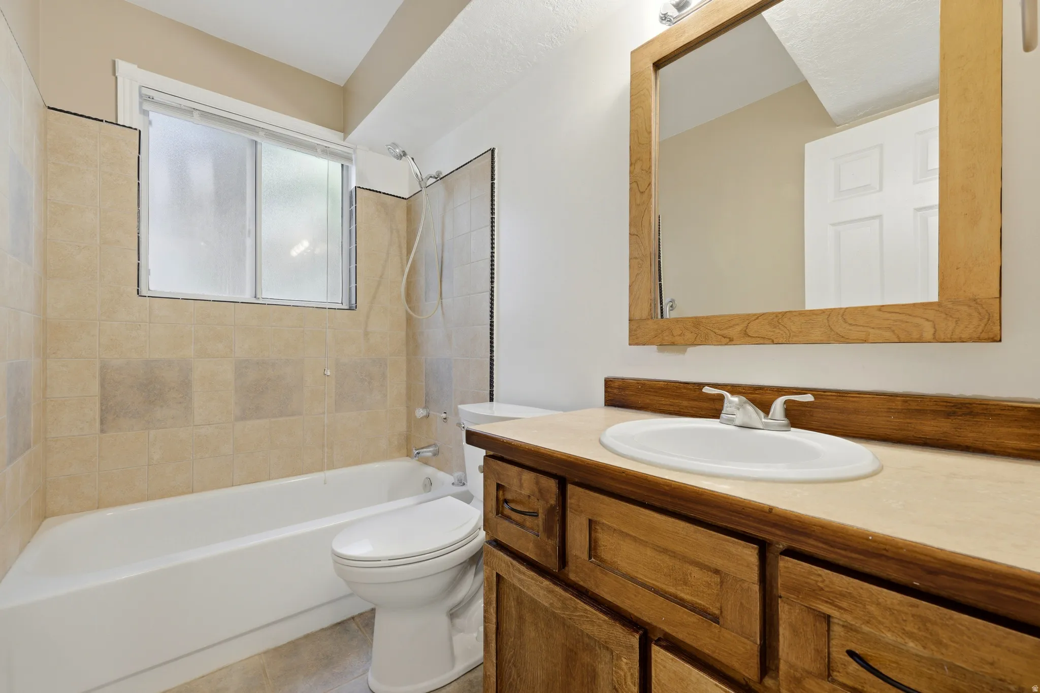 Built-in vanity with a drop-in sink, natural wood-finish cabinetry, and a framed mirror