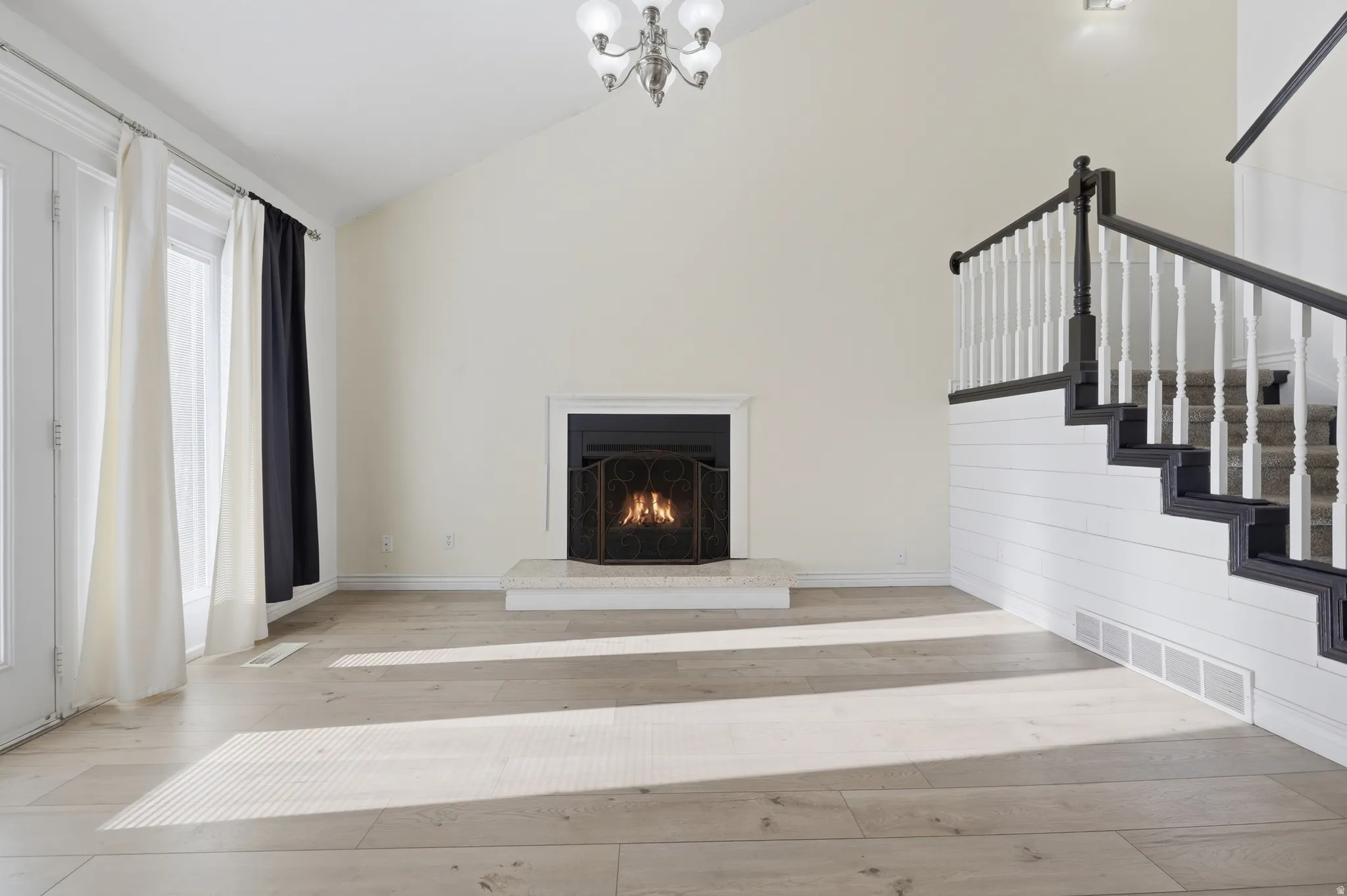 Vaulted ceiling, wood-finish flooring, fireplace with stone hearth, double French doors, and a staircase with a white spindle railing