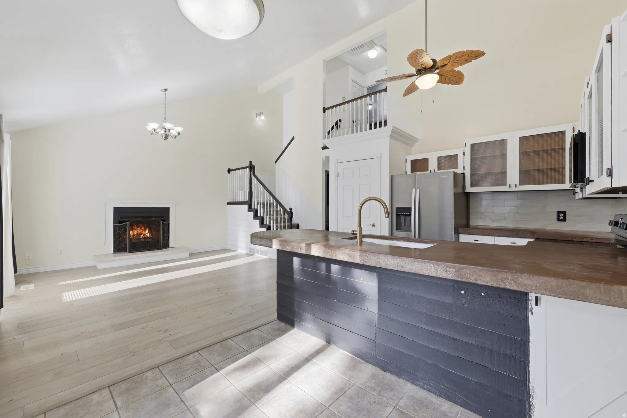 Open-concept living area featuring a wood-finish plank floor, a gas fireplace with surround, and a chef's kitchen with a large island topped in wood-finish countertops, white cabinetry with glass-front upper storage, stainless steel appliances, and an und