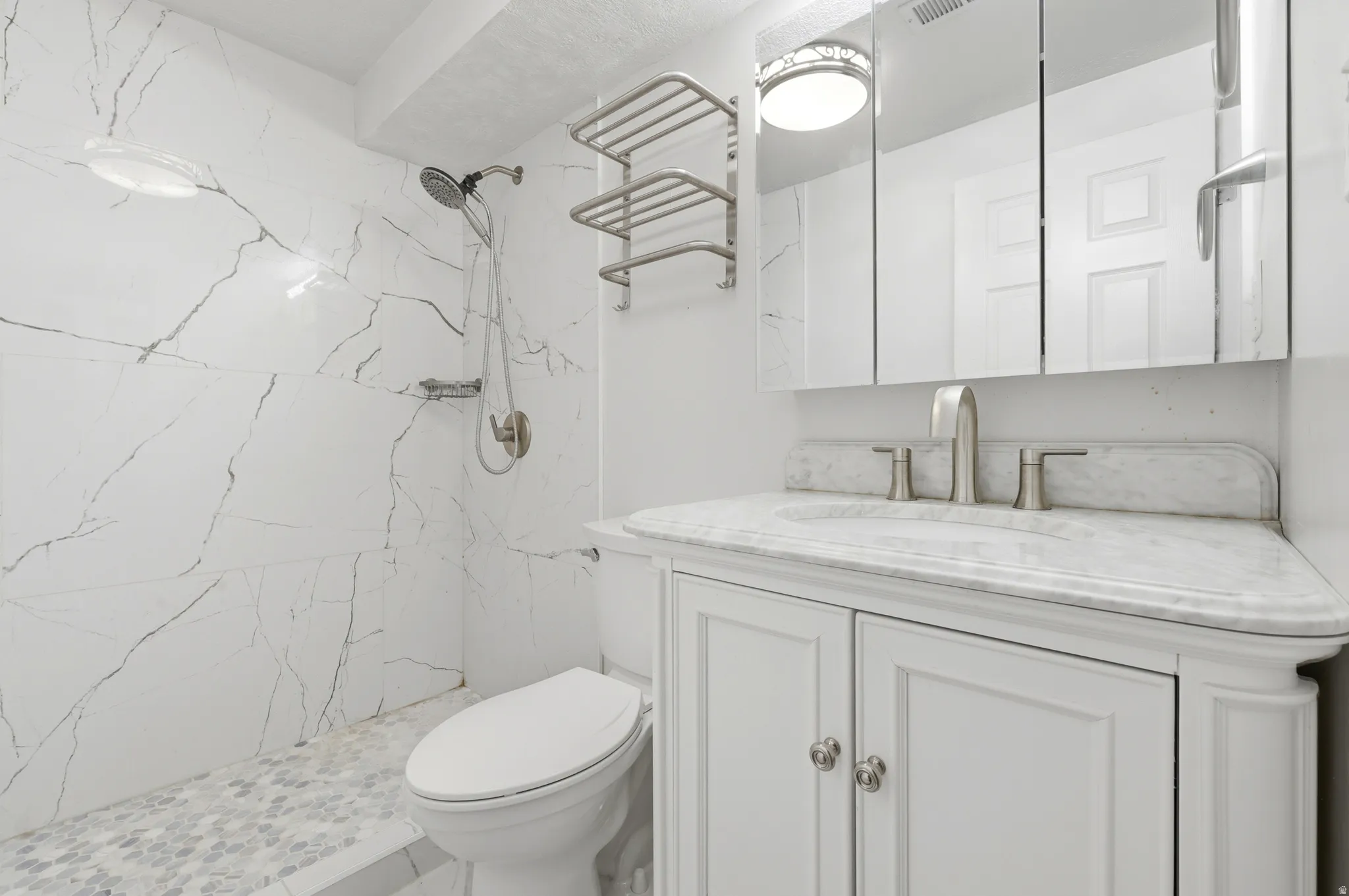 Spa-inspired bathroom featuring marble-look tile wall surround with linear detailing, white vanity cabinetry with dual handles, marble-finish countertop, polished nickel fixtures, recessed ceiling lighting, and hexagonal tile flooring
