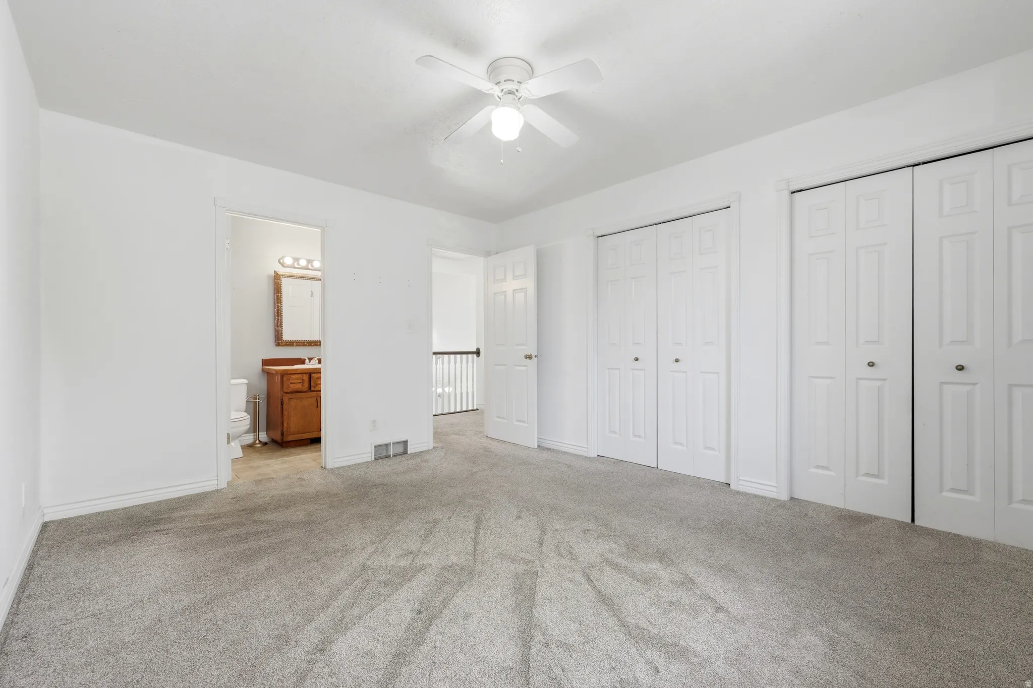 Spacious bedroom featuring neutral carpeting, ceiling fan with integrated lighting, and an abundance of natural light from multiple windows