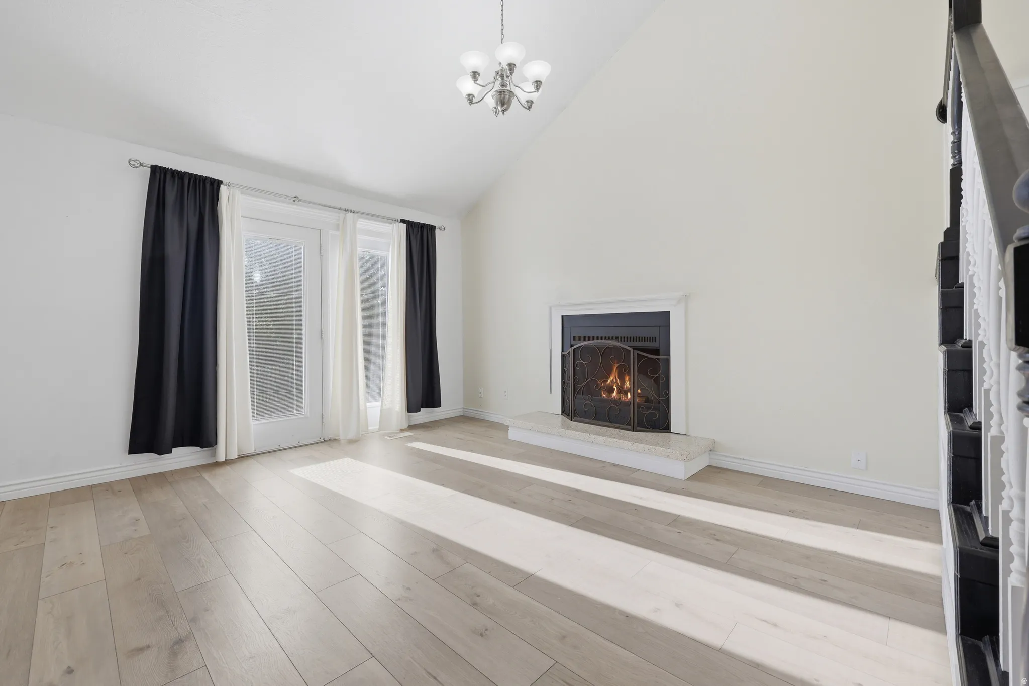 Vaulted ceiling, wood-finish flooring, fireplace with hearth, double French doors, and a chandelier