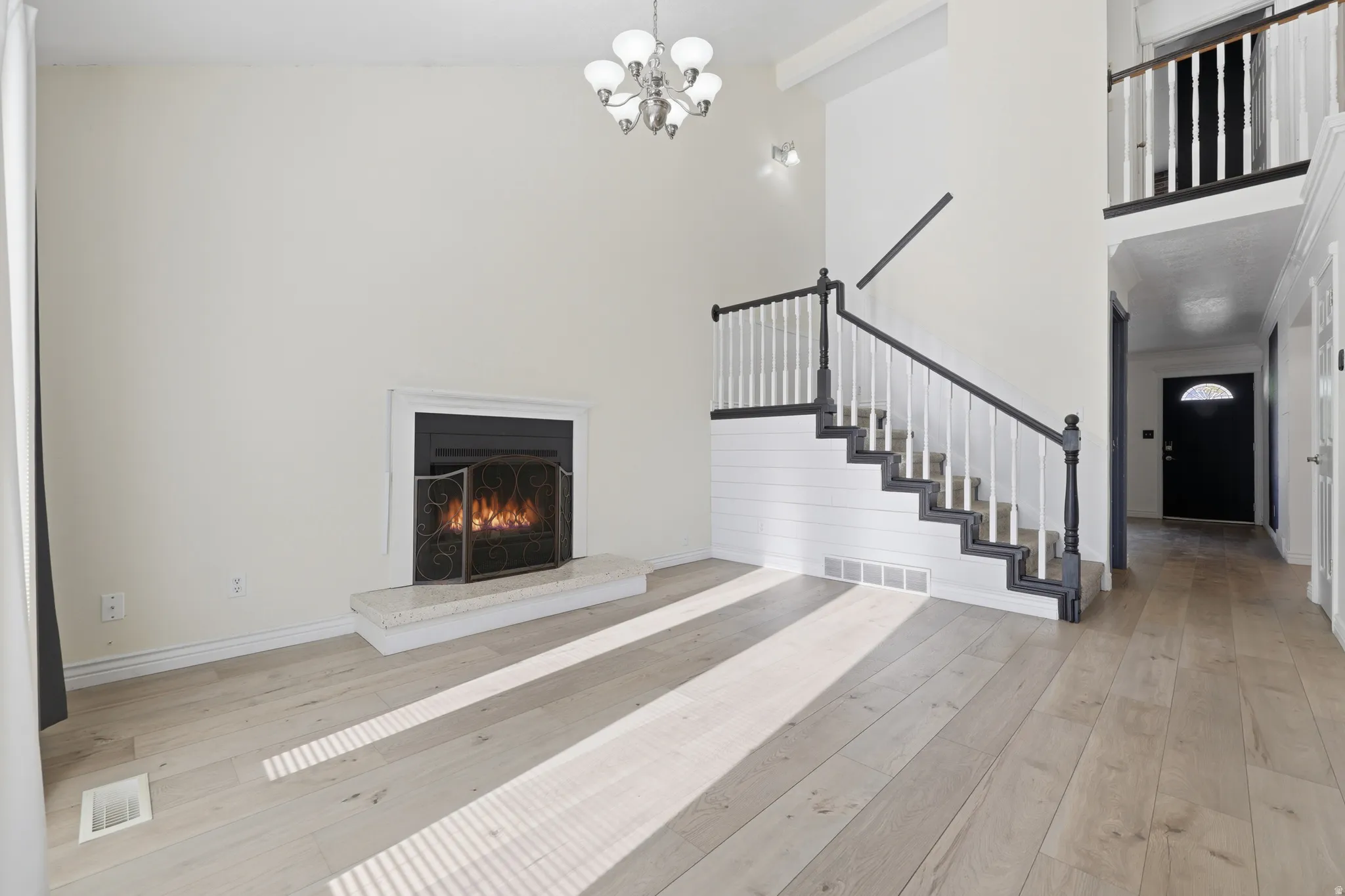 Hardwood flooring throughout, a gas fireplace with a stone hearth, a two-story ceiling, and a staircase with painted newel posts and balusters