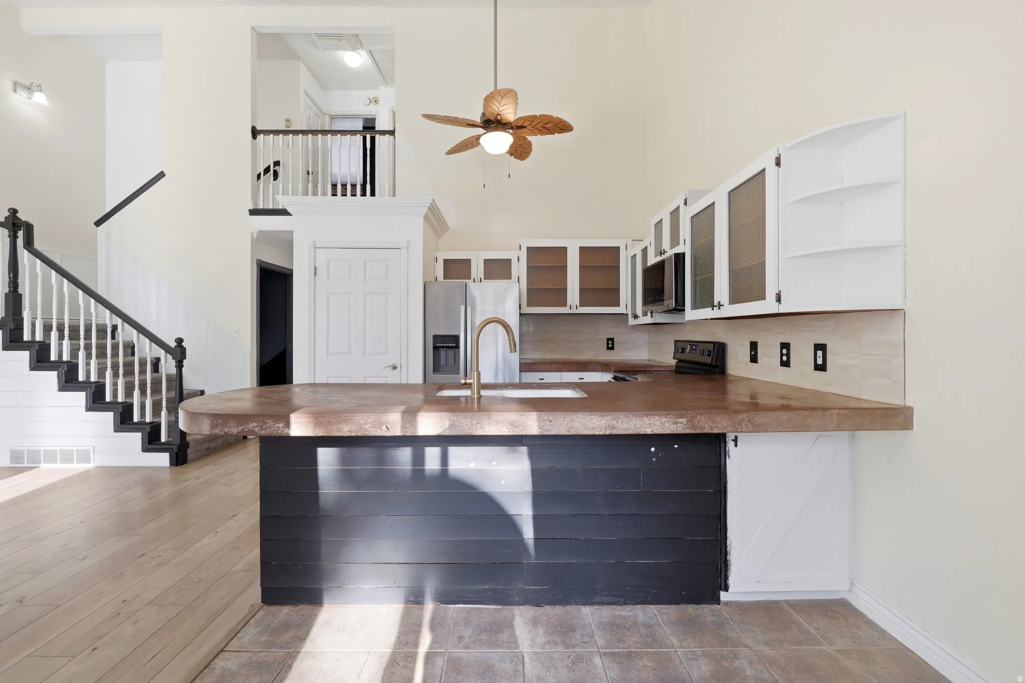 Vaulted ceilings, a dark wood-finish staircase with white balusters, kitchen with stainless steel appliances, white cabinetry, and a central island with a concrete countertop