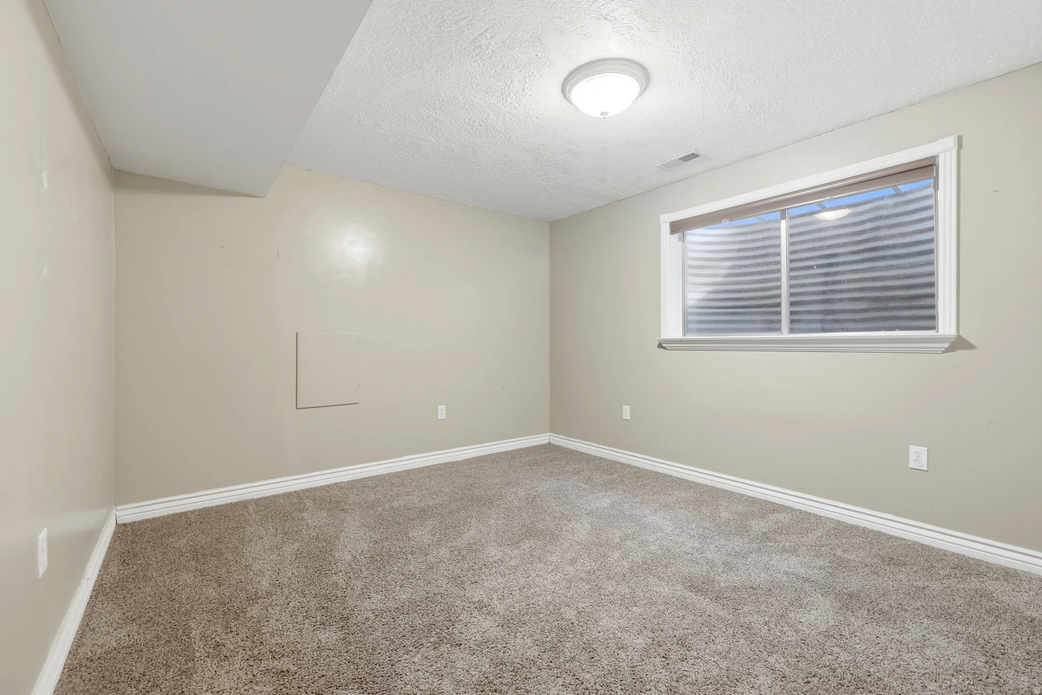 Spacious bedroom with neutral wall finishes, plush carpet flooring, and abundant natural light from a large horizontal window