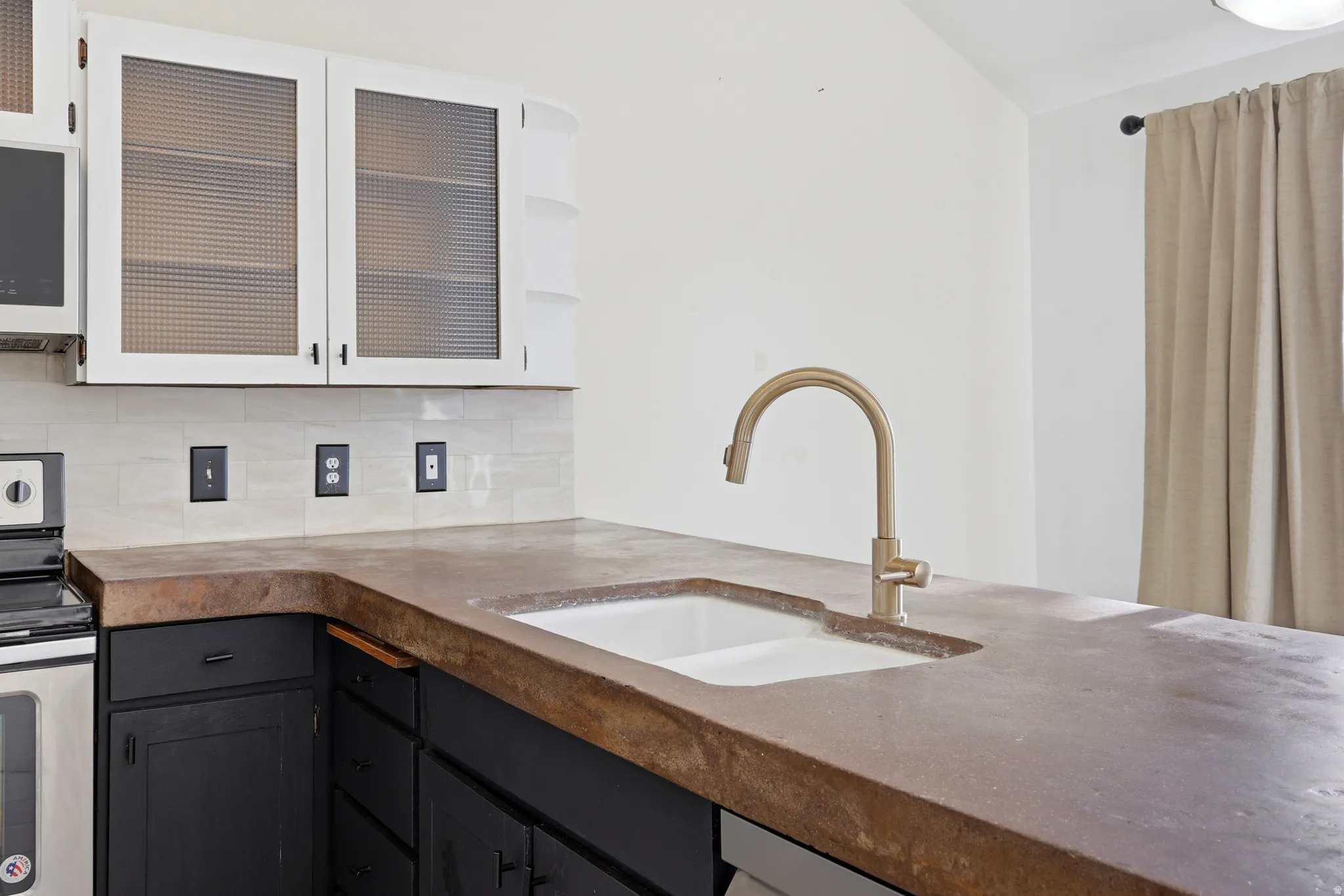Modern kitchen island featuring warm wood-finish countertops, an undermount sink with bronze gooseneck faucet, white cabinetry with integrated glass-front upper storage, and black lower cabinetry with ample workspace for meal preparation and entertaining