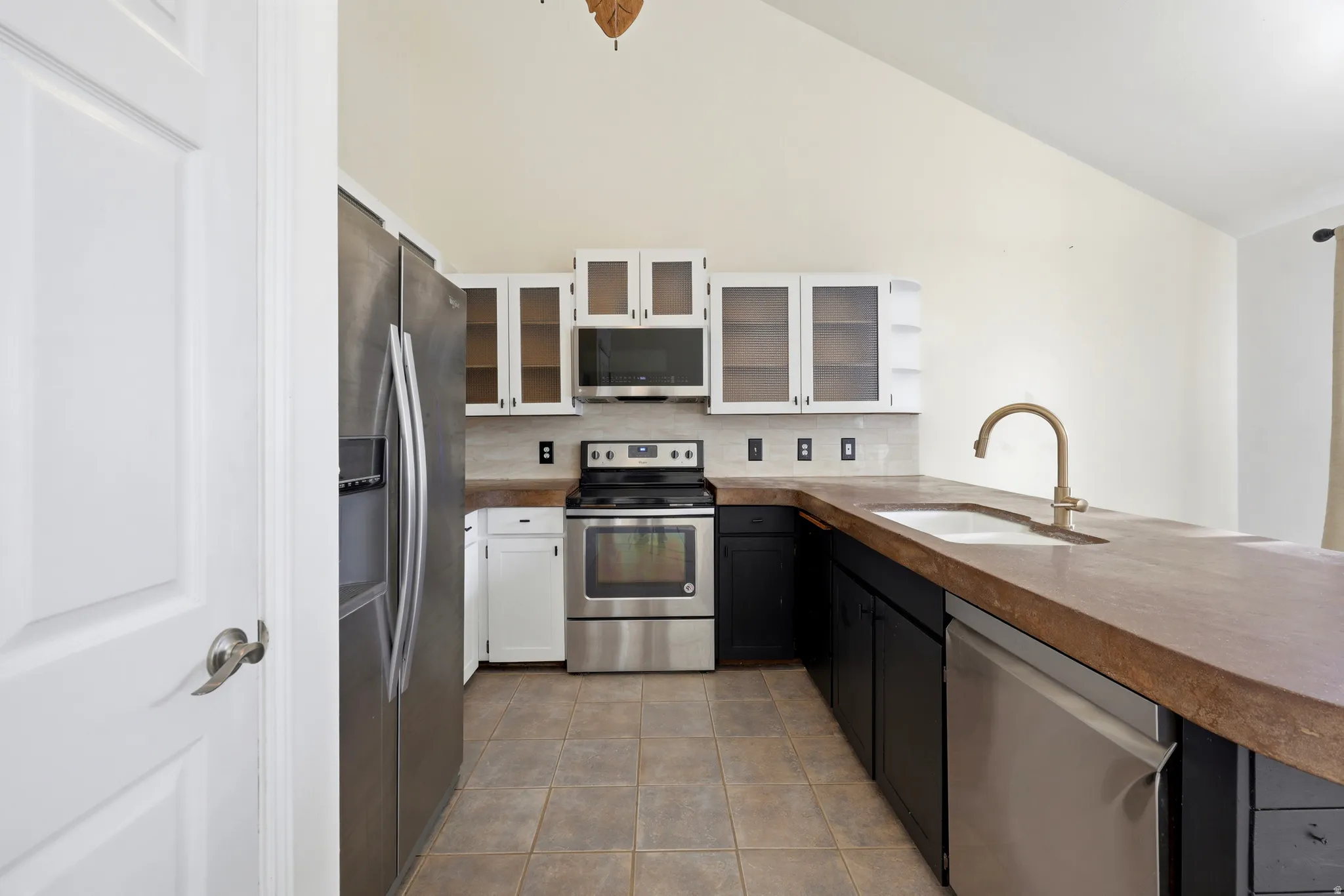 Vaulted ceiling, stainless steel appliances, tile flooring, glass-front upper cabinetry, and a single-basin sink with a gooseneck faucet