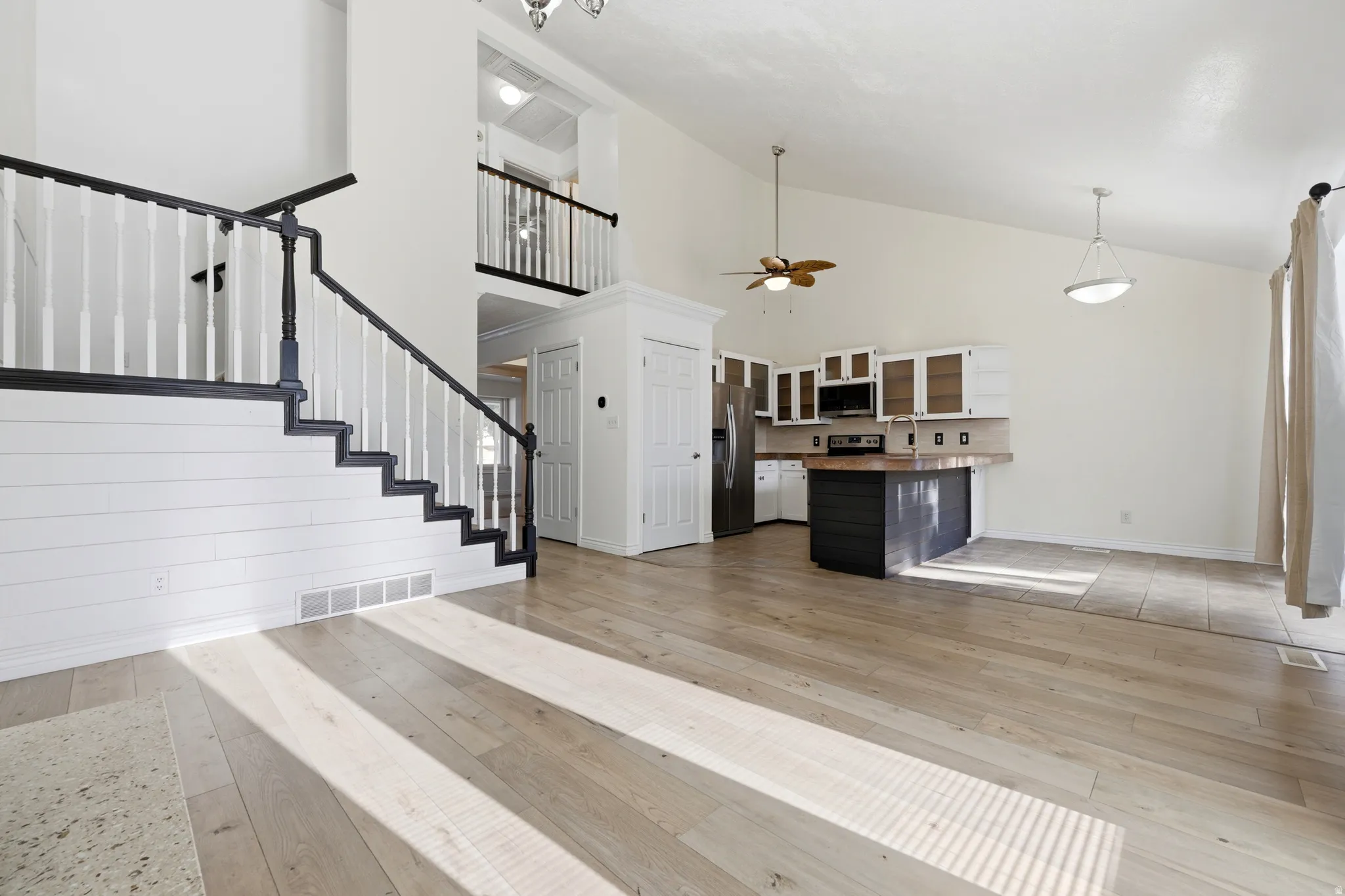 Vaulted ceilings, wood-finish flooring, kitchen island with seating, stainless steel appliances, and white shiplap wall accent