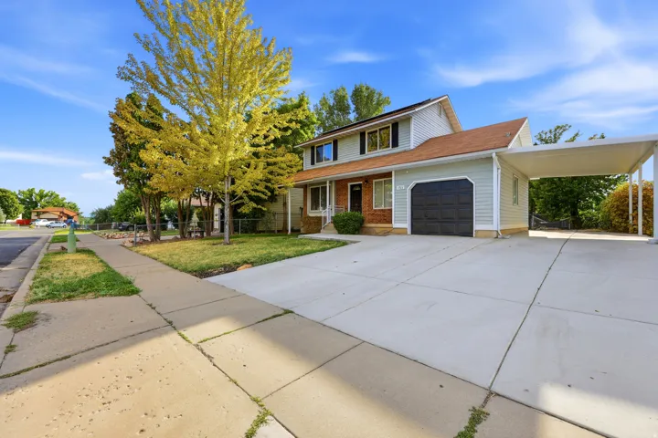 Two-story residence featuring light blue siding with brick accents, an attached garage, and a covered carport