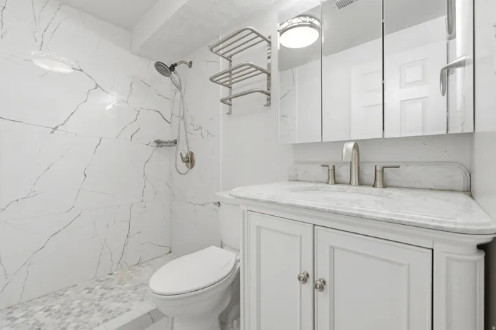 Spa-inspired bathroom featuring marble-look tile wall surround with linear detailing, white vanity cabinetry with dual handles, marble-finish countertop, polished nickel fixtures, recessed ceiling lighting, and hexagonal tile flooring
