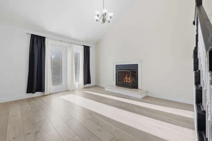 Vaulted ceiling, wood-finish flooring, fireplace with hearth, double French doors, and a chandelier