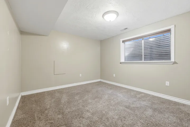 Spacious bedroom with neutral wall finishes, plush carpet flooring, and abundant natural light from a large horizontal window