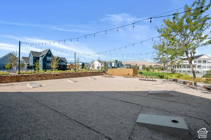 Expansive outdoor common area featuring a gravel surface, string lighting, built-in cornhole boards, and wood seating areas