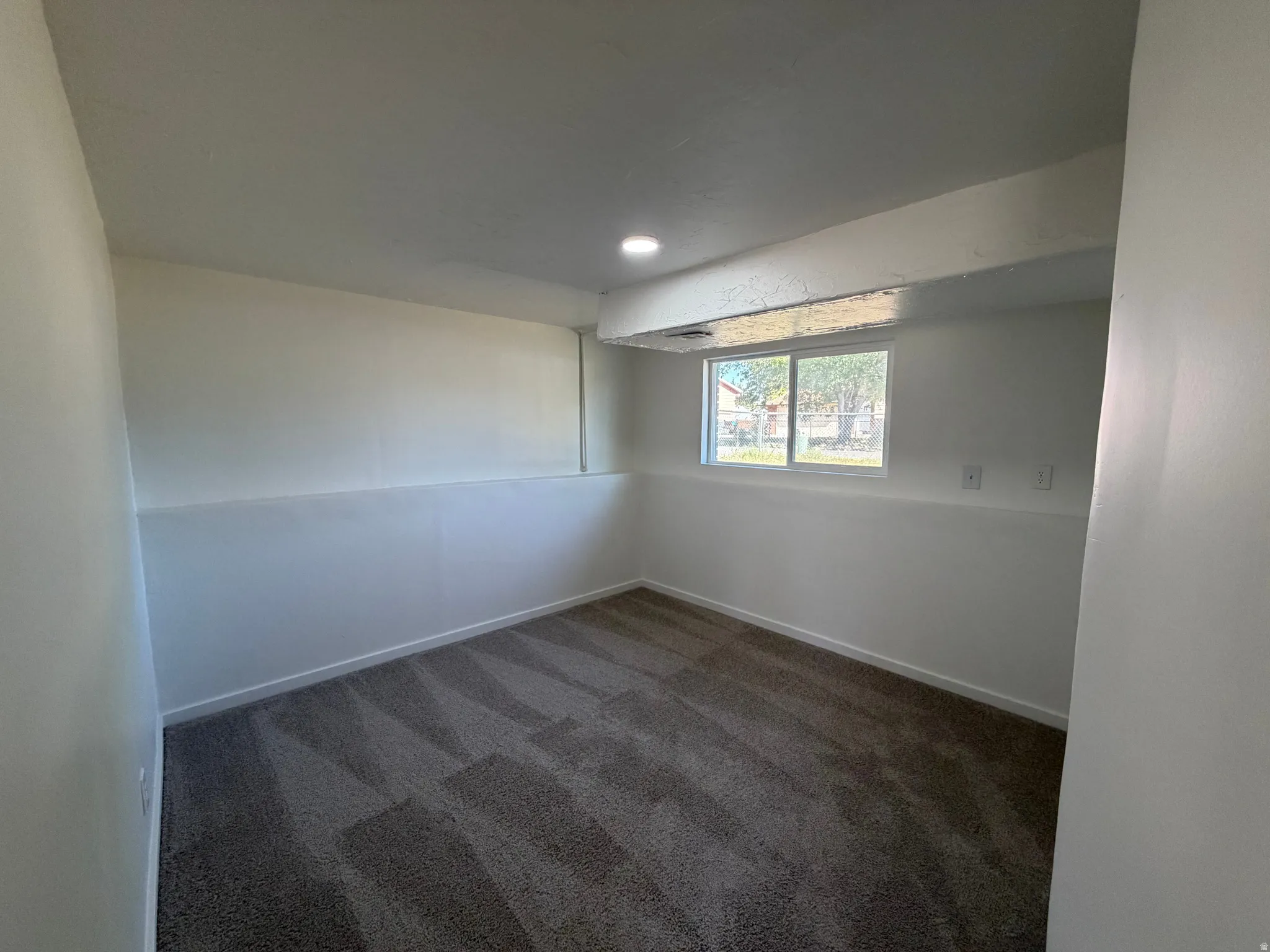 Recessed ceiling lighting, patterned carpet flooring, white walls, and a window