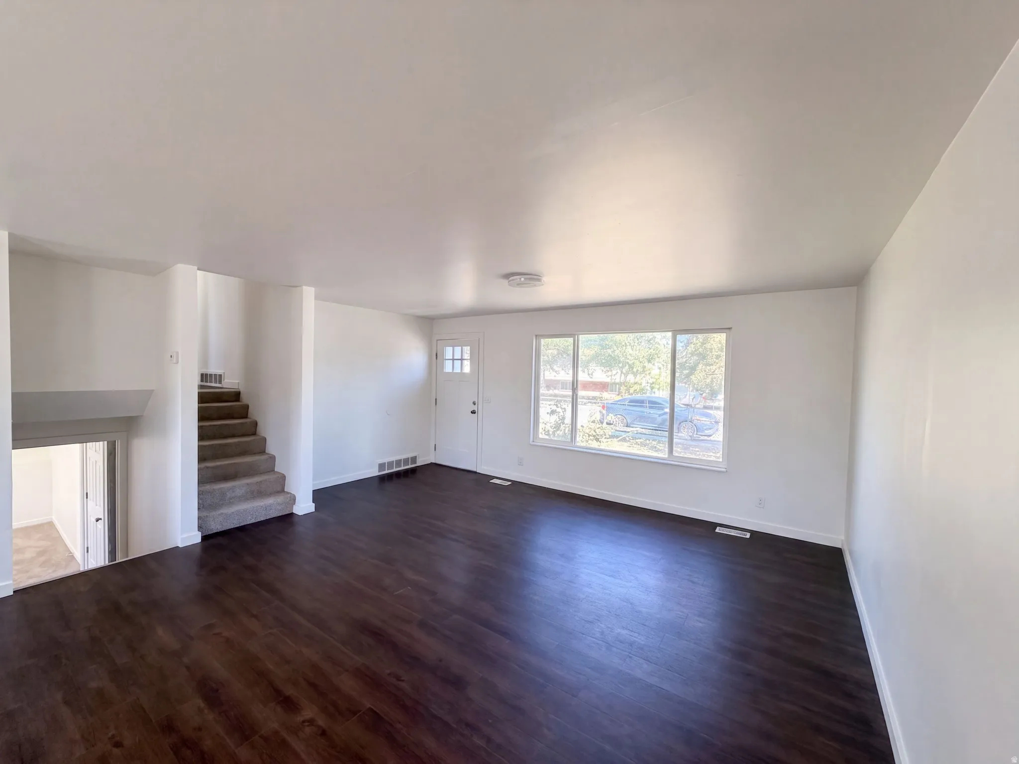 Dark wood-finish flooring, white walls, and a large window with white trim