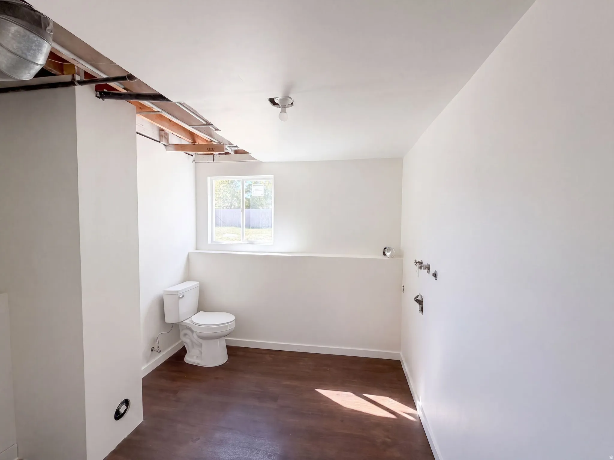 Window with natural light, finished concrete flooring, exposed ceiling joists, and a partial wall structure