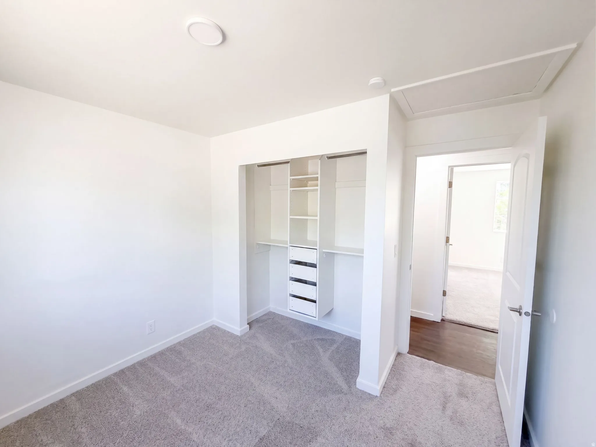 Recessed ceiling light, built-in closet organization system with shelving and drawers, neutral-toned carpeting, white interior doors, and attic access panel