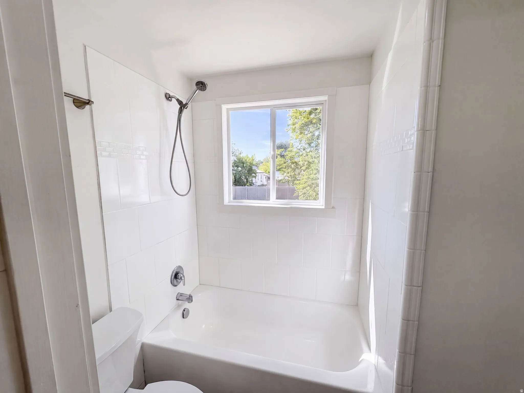 White subway tile shower surround with an accent band, white bathtub, chrome shower fixtures, and a white framed window