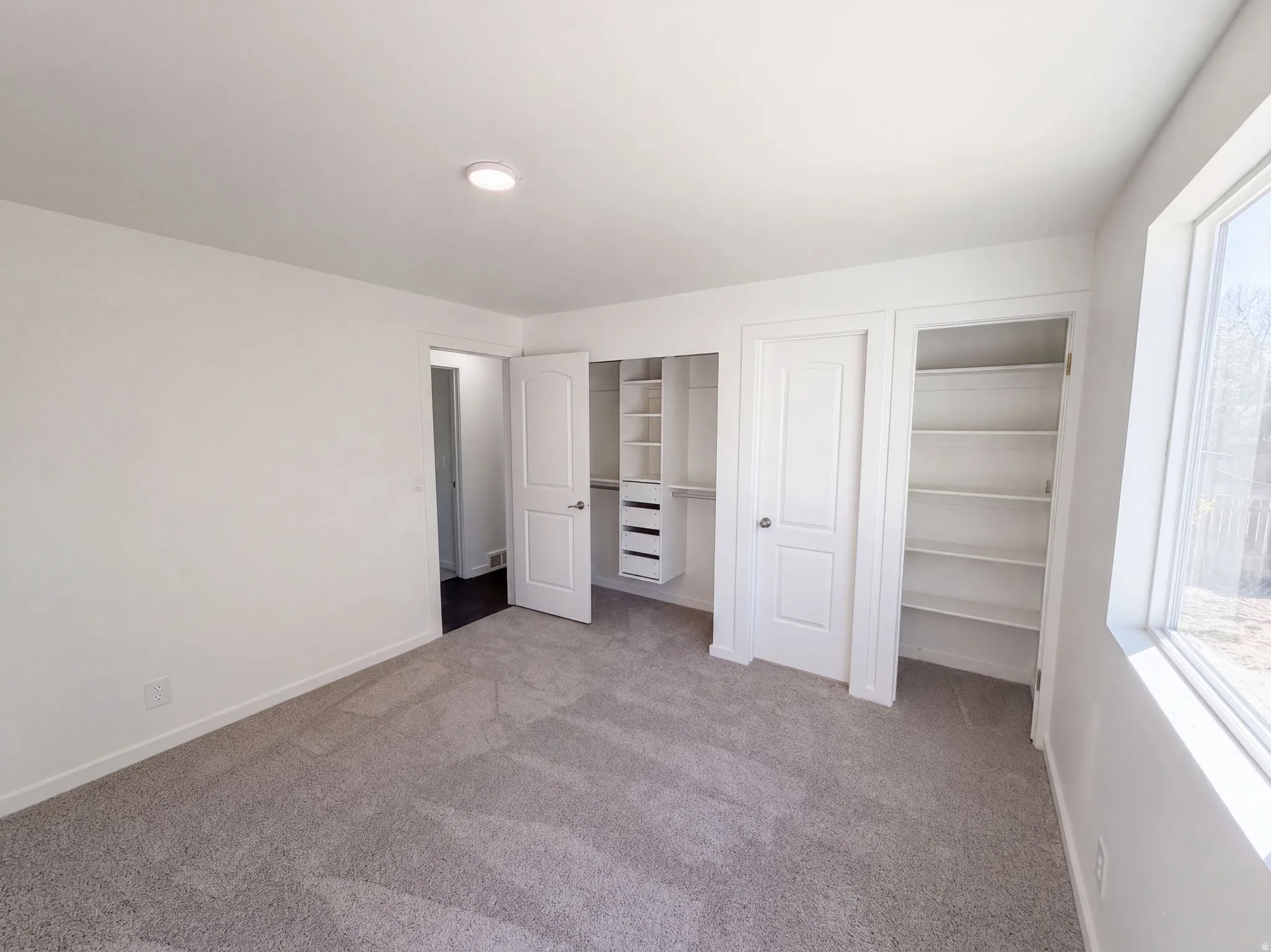 Plush carpet flooring, recessed ceiling lighting, built-in shelving, organized closet system, and a large window