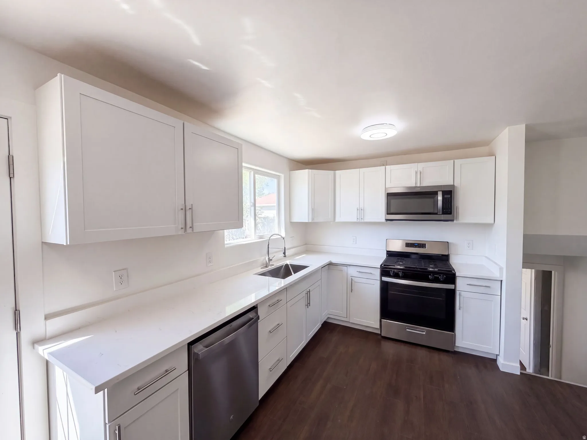 Kitchen featuring white shaker-style cabinetry, stainless steel appliances, a stainless steel sink, light-toned countertops, and wood-finish flooring