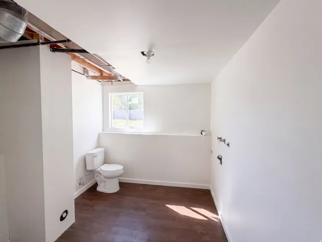 Window with natural light, finished concrete flooring, exposed ceiling joists, and a partial wall structure
