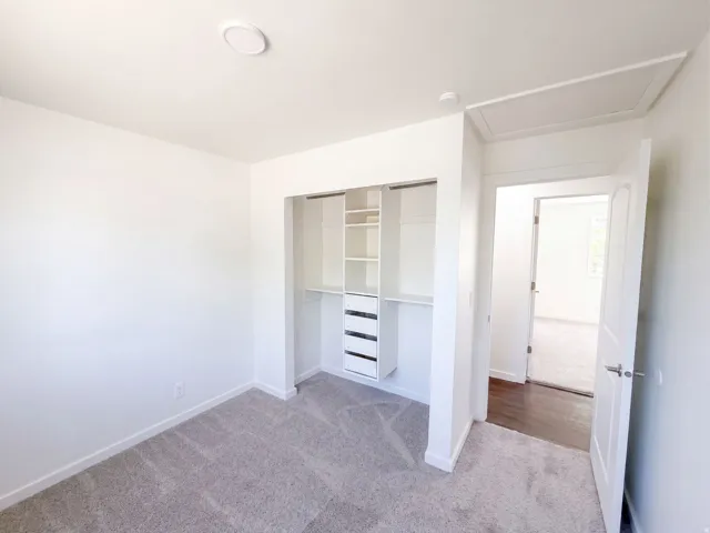 Recessed ceiling light, built-in closet organization system with shelving and drawers, neutral-toned carpeting, white interior doors, and attic access panel