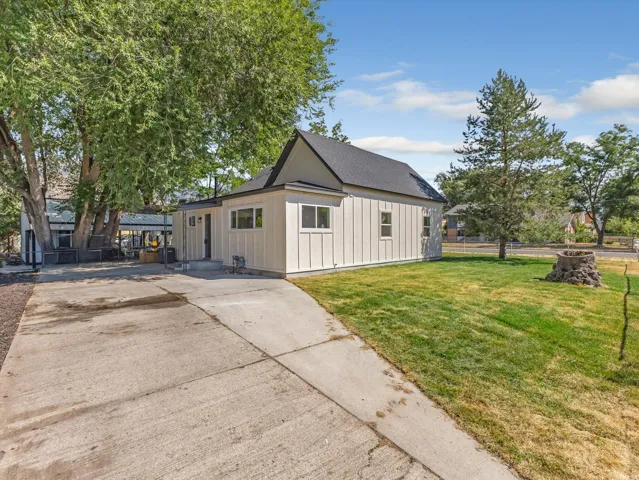 Contemporary board and batten siding, dark shingle roof, concrete driveway, mature landscaping, and a well-maintained lawn