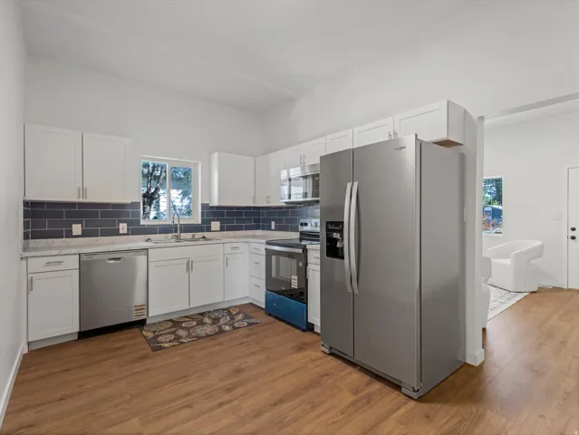 Kitchen featuring wood-finish flooring, white cabinetry, dark subway tile backsplash, and stainless steel appliances