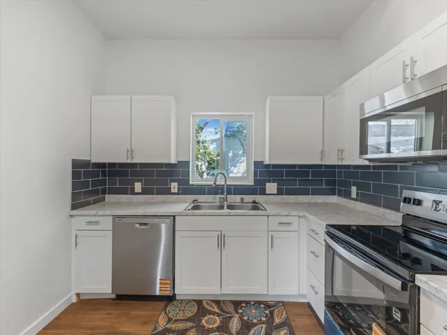 White cabinetry, stainless steel appliances, dark subway tile backsplash, light countertops, and wood-finish flooring